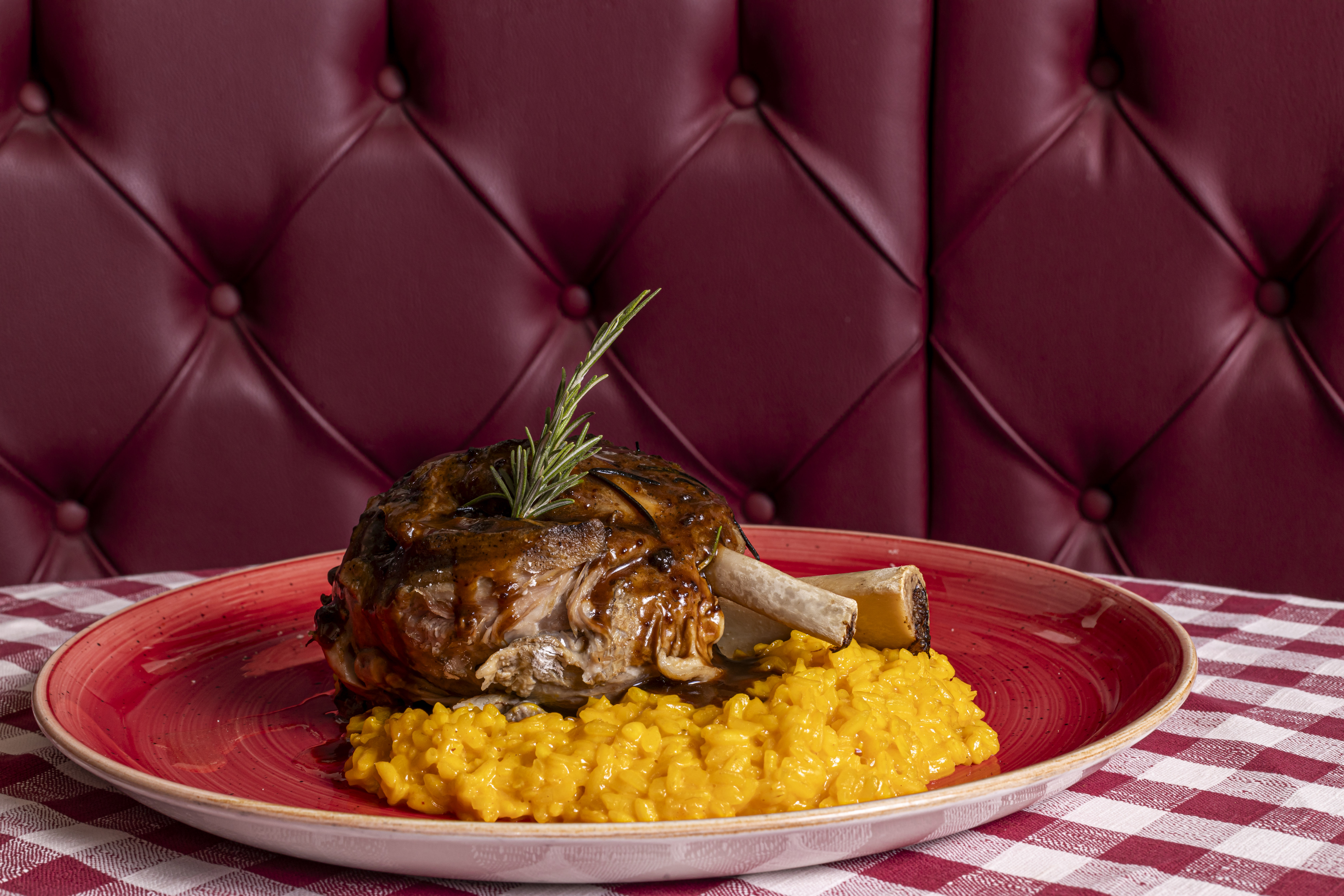 Ossobuco di vitello stufato servito su un letto di risotto alla milanese (zafferano) nel piatto rosso della Taverna del Borgo Antico.